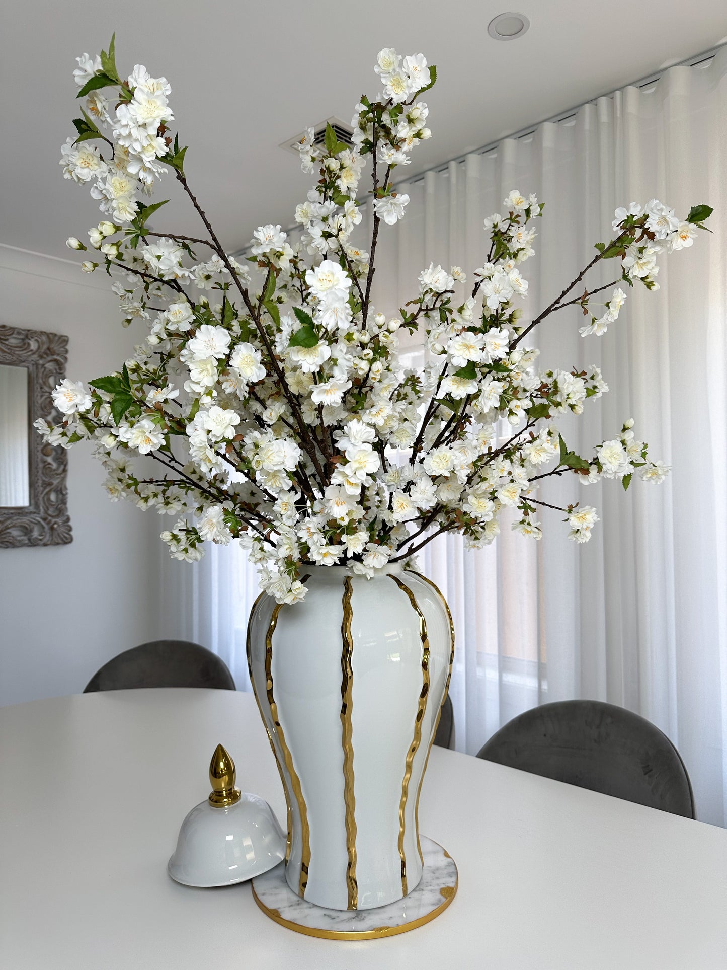 10 white cherry blossom stems in white and gold vase on marble board on dining table front view