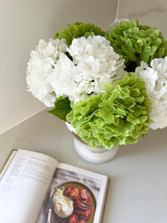 Top angled view of real touch white and green hydrangeas on kitchen bench with recipe book