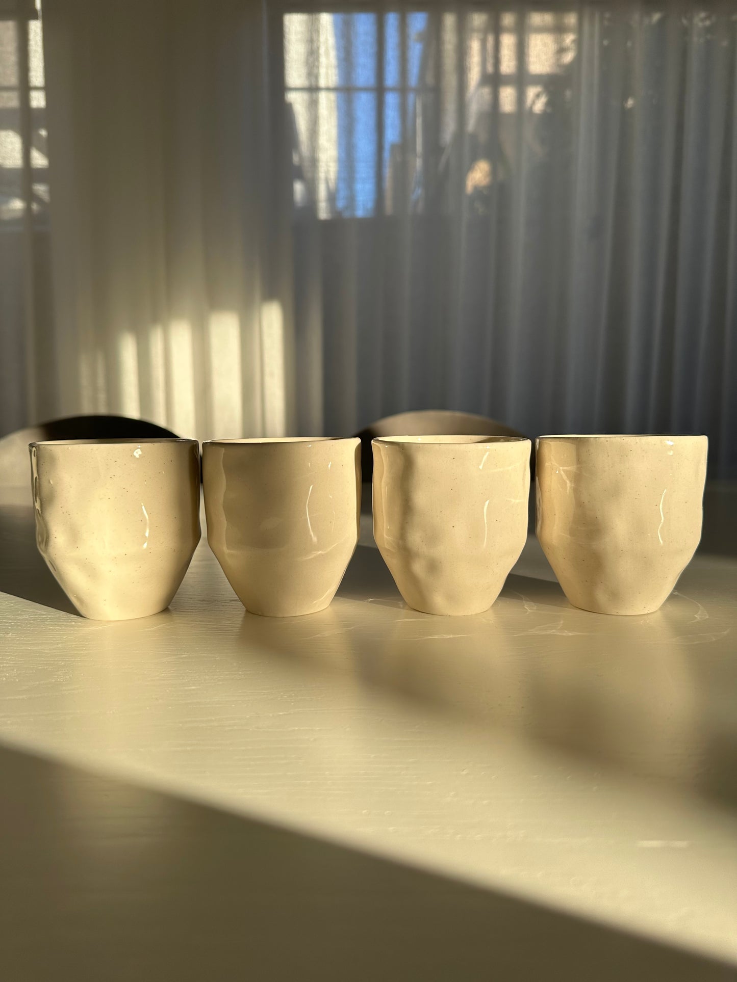 Set of 4 coffee mugs wabi sabi styled in early morning sunlight on dining table from front view