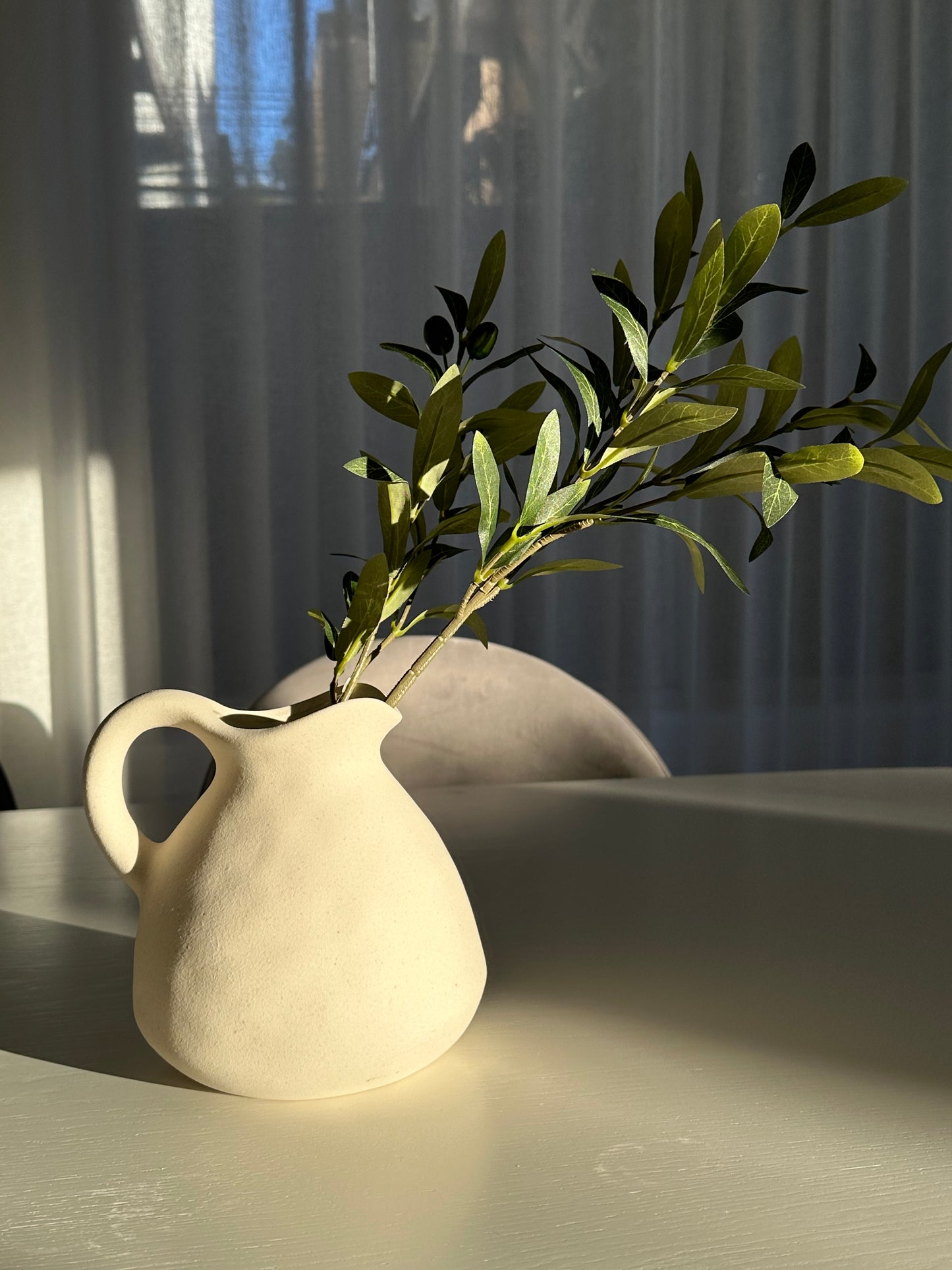 White modern vase in morning sunlight with earthy textures and tones with an olive branch in it - 1 vase