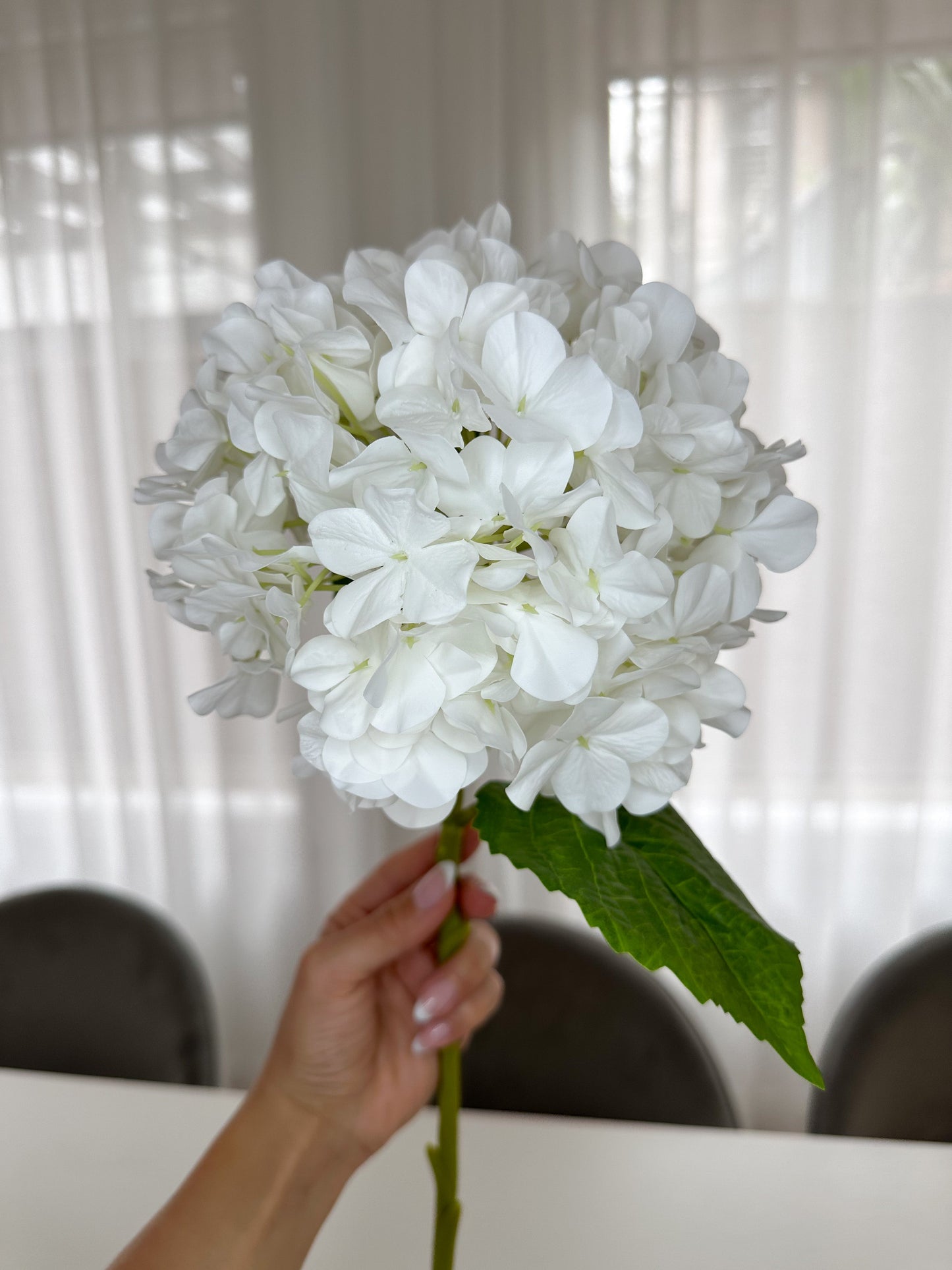 White Real Touch hydrangea stem singular held by single hand