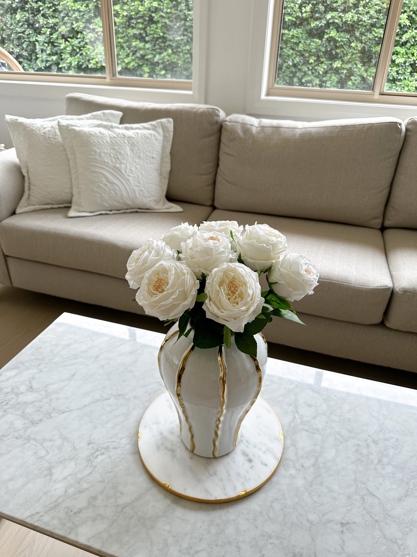 White and Gold striped ceramic vase with white real touch peony stems in it. Top angled view of the product on the coffee table.