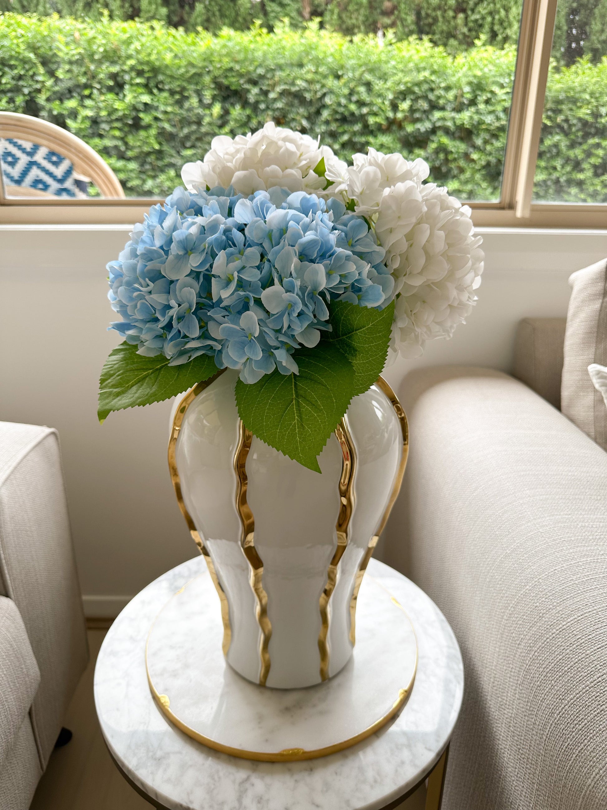 White and Blue Silk and Real Touch Hydrangea Stems in white and gold vase up close from front angle on marble board